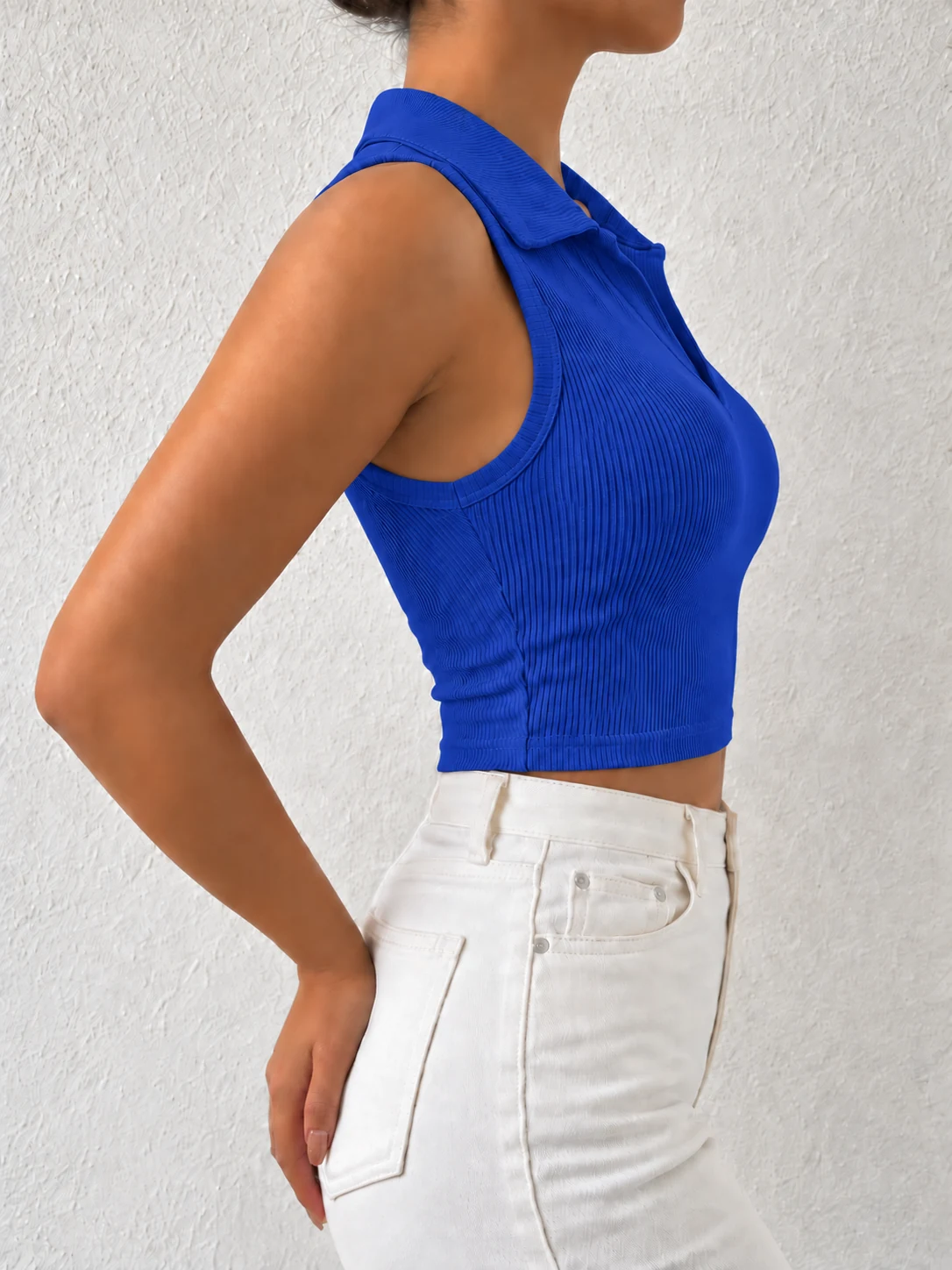 Side view of a royal blue sleeveless ribbed polo crop top with white denim